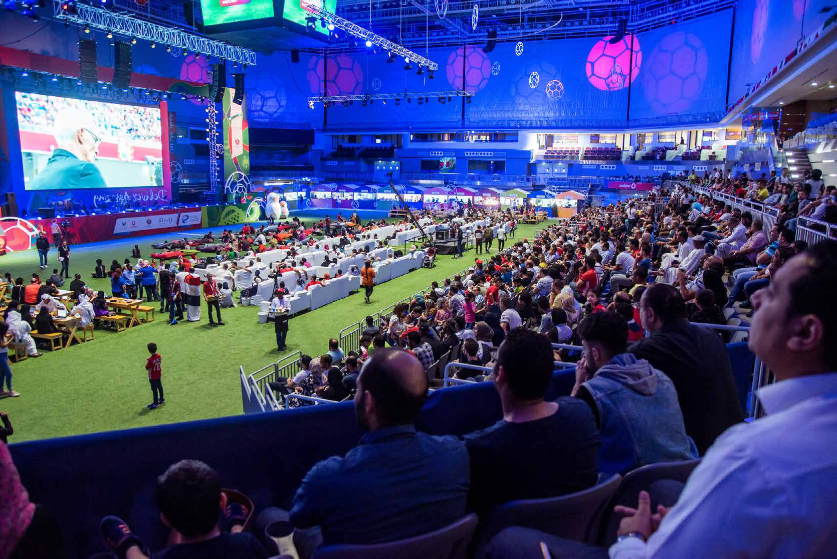 Spectators filling a covered fan zone watching a match on a large LED screen
