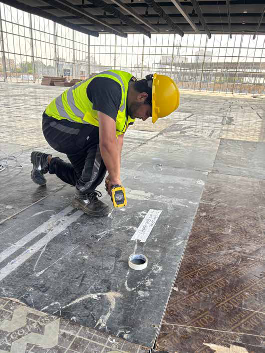 Engineer marking out cable routing on the floor of a festival venue under construction