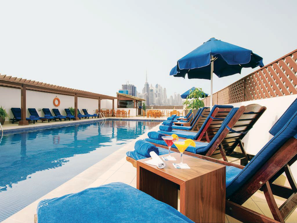 Rooftop pool deck at a Citymax hotel with sun loungers and the Dubai skyline behind