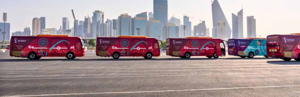 Fleet of branded tournament shuttle buses parked in a row with the Doha skyline behind